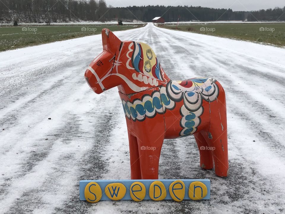 Greetings from Sweden with a Dalecarlian horse and a yellow painted stones on a snow covered road

