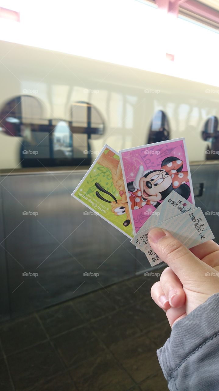 Tickets in hand for Disneyland at Japan Tokyo  Disneyland. A ticket of Minnie and plot with two train tickets. The Mickey mouse ears on the train in the back