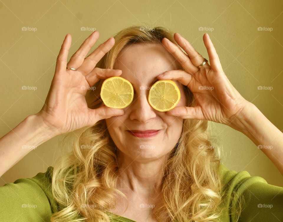 Selfie of a blonde woman holding lemon slices over her eyes