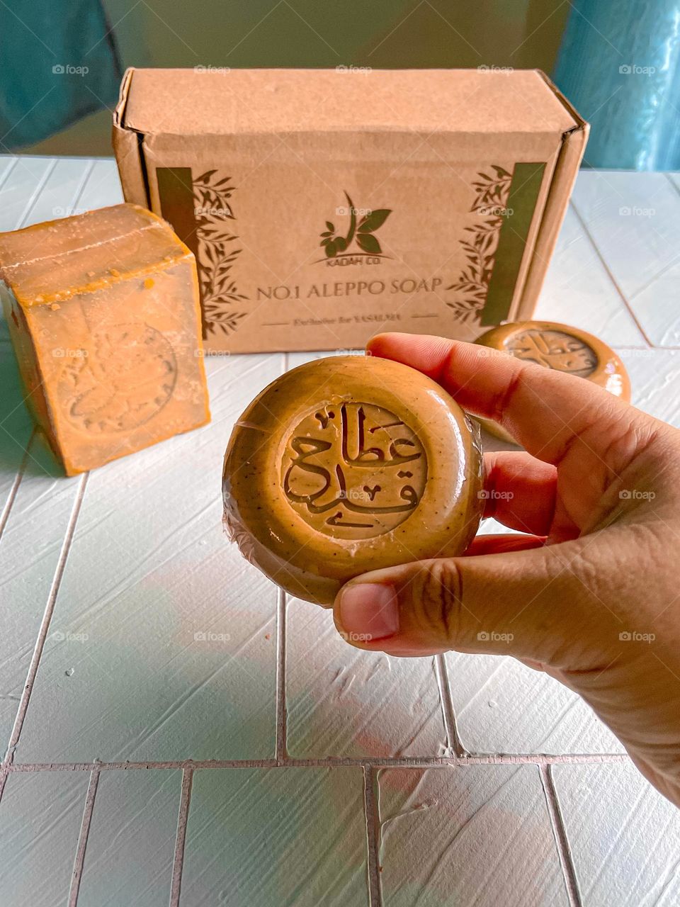 A hand holding an olive soap, earthy brown in colour with arabic text written on the soap