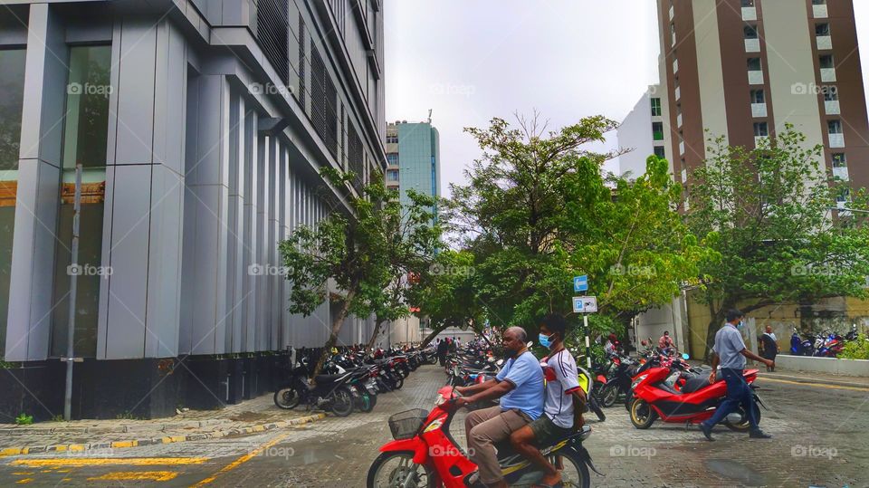 Men on scooter along with numerous parked scooter in the street of Malè, Maldives