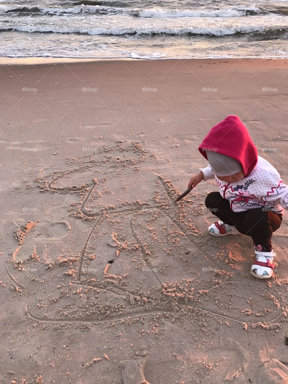 Baby draw on a beach sand in the evening 