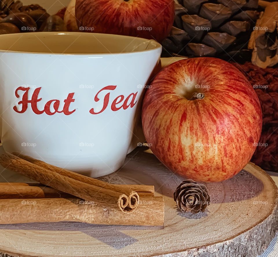 Hot apple & cinnamon tea on wood platter, with fruit, spices and pine cones 