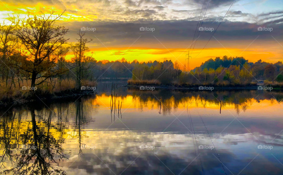 Colorful and dramatic sunrise or sunset sky over a forest lake, with reflections in the water