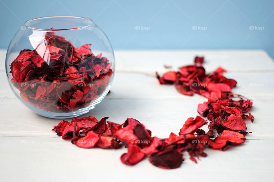 Rose petals on white table and clear vase filled with dried petals