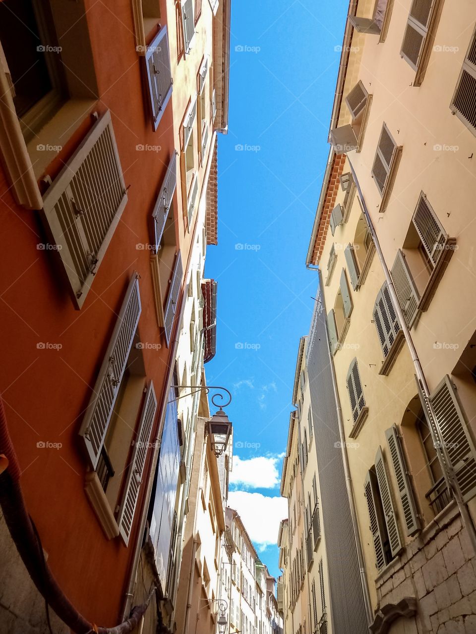 narrow street of the old town in France, windows with shutters, lantern, blue sky