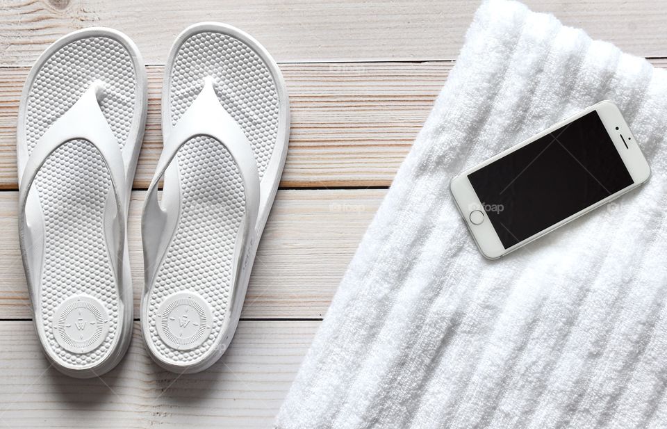 Electronics, white cell phone, white flip flops and white beach towel 