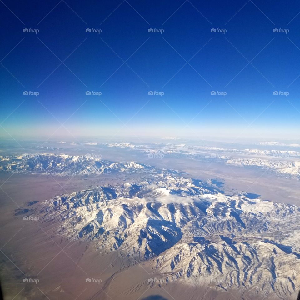 airplane view of snow covered mountain peaks with a blue sky
