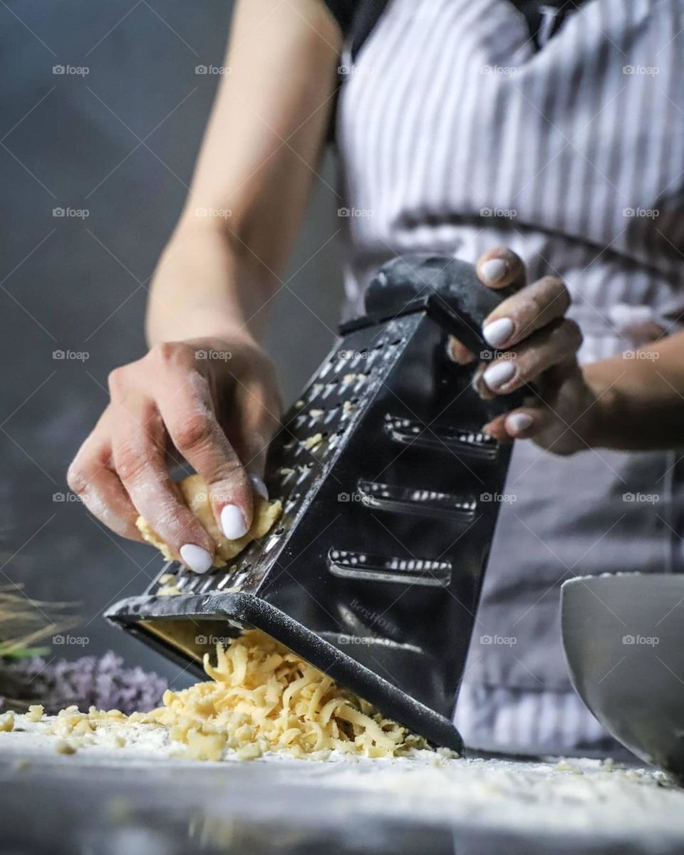 A girl in a chef's uniform in the kitchen rubs the future dough for a honey cake on a grater on the table flour and purple flowers