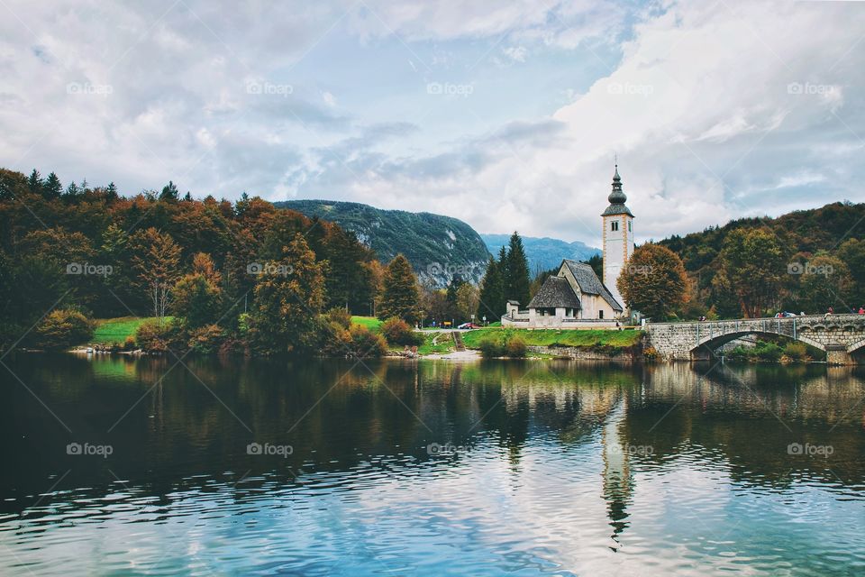 Wallpaper of scenic view of the autumn mountains landscape and church against the blue lake Bohinj. Slovenia.