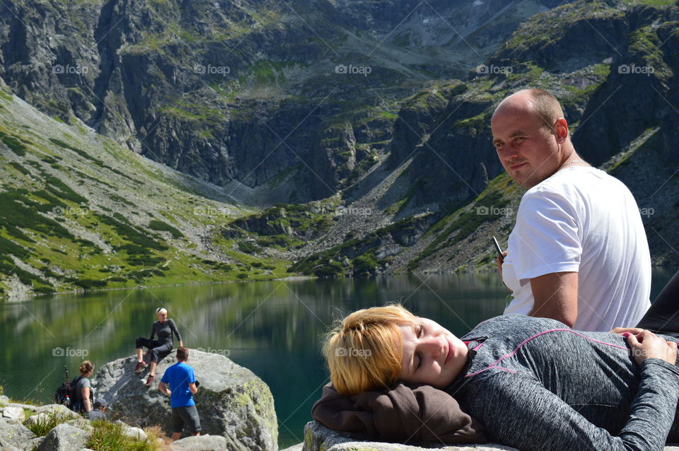 Man sitting beside the woman sleeping near the lake