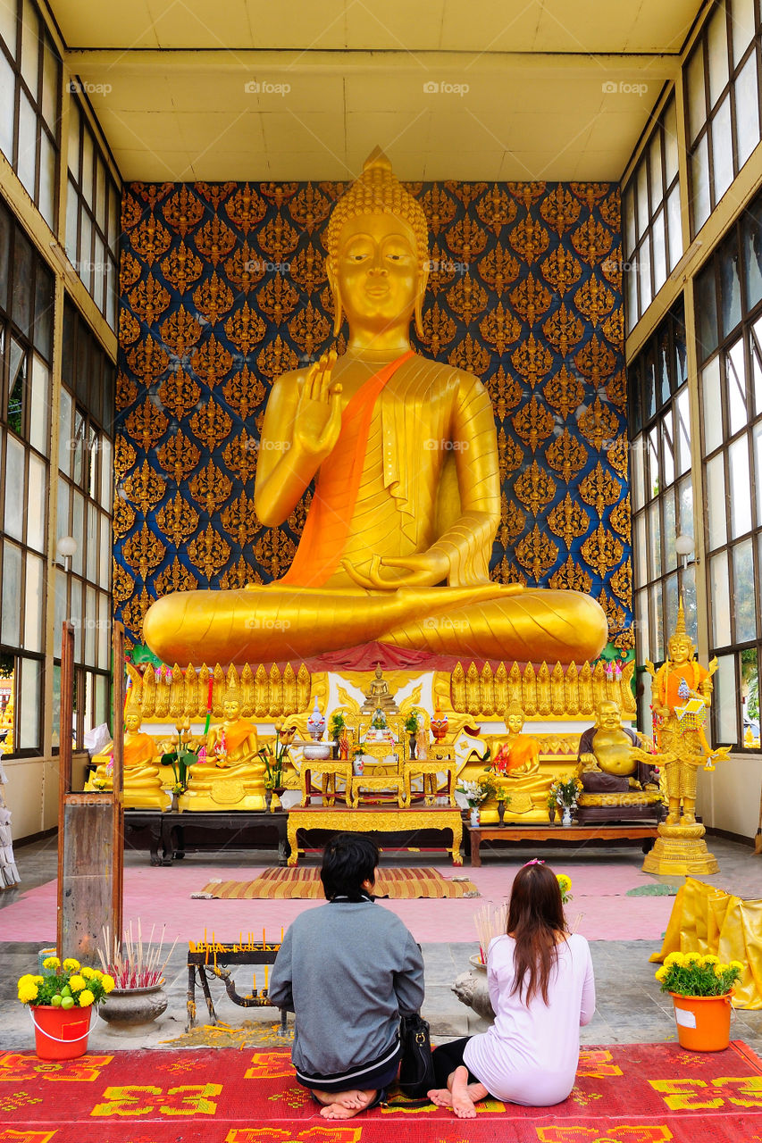 MUKDAHAN, THAILAND -APR 24, 2011 Young couple are worshiping the golden Buddha at a temple in Mukdahan Province, Thailand.
