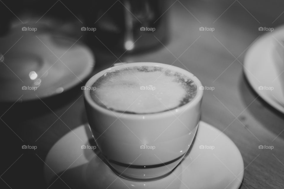 A black and white portrait of a cup of coffee with white milk cream on top of it.