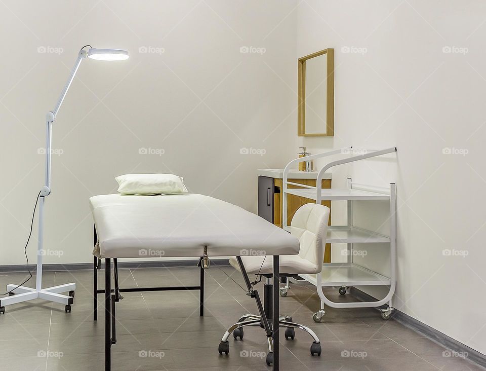 White interior of a modern cosmetology room in a beauty salon. Cosmetologist's workplace with a couch and professional lighting. Contemporary treatment room. Horizontal orientation