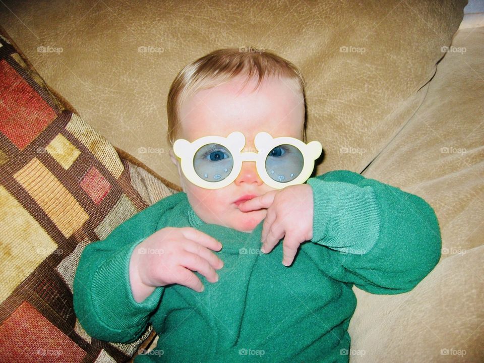 Darling sweet little boy lounging in couch with silly yellow circular sunglasses on! 