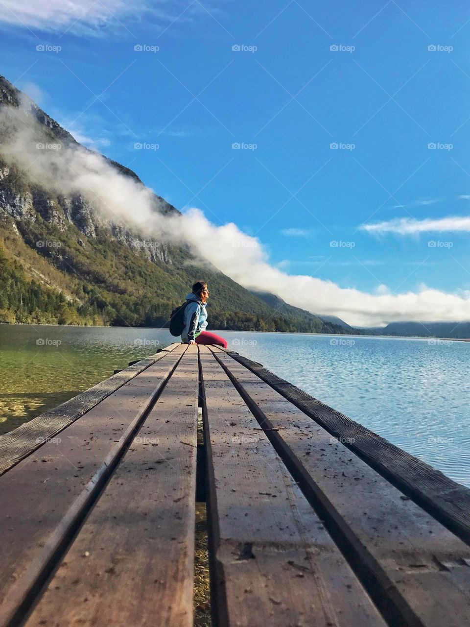 Young woman sitting near the river at the Alps mountains in autumn season in foggy morning