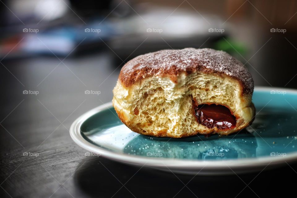 A brown baked donut with rosehip jam and sugar lies half-eaten on a blue plate 