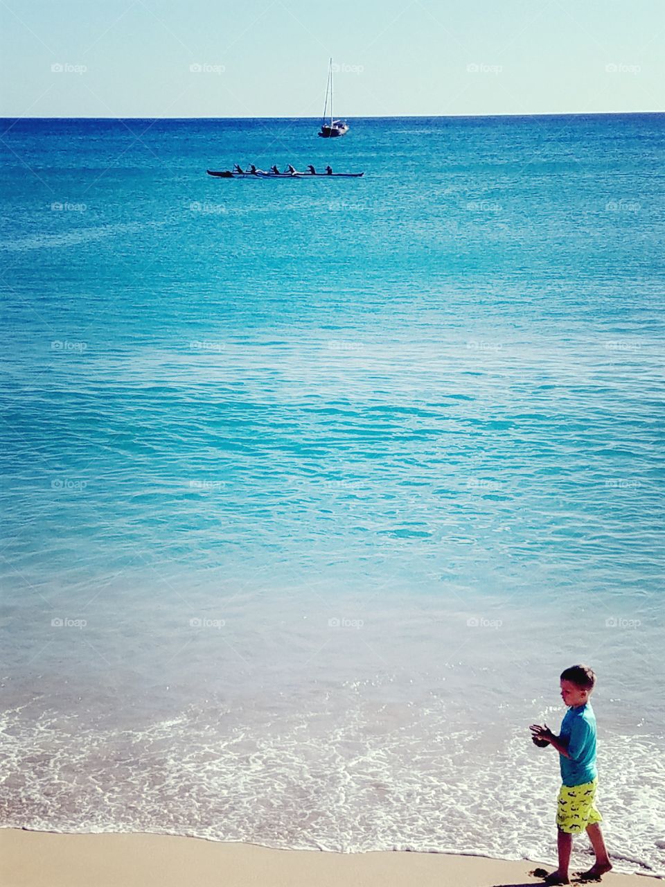 Boy on beach with boats cruising through Pokai Bay