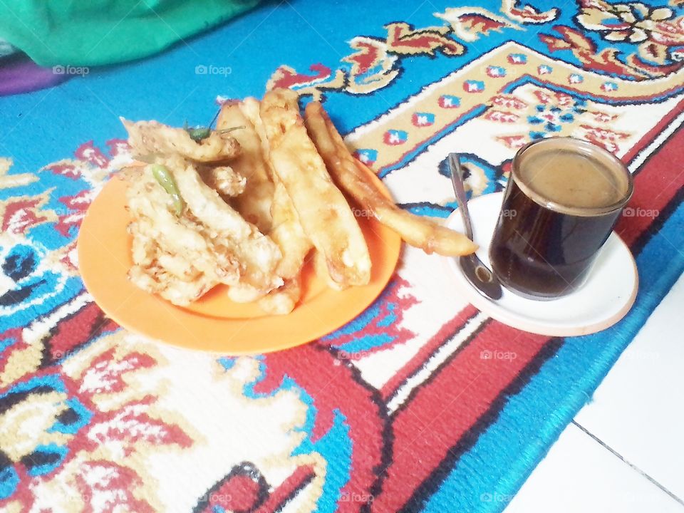 Drinking warm black coffee accompanied by fried bananas and vegetable bakwan