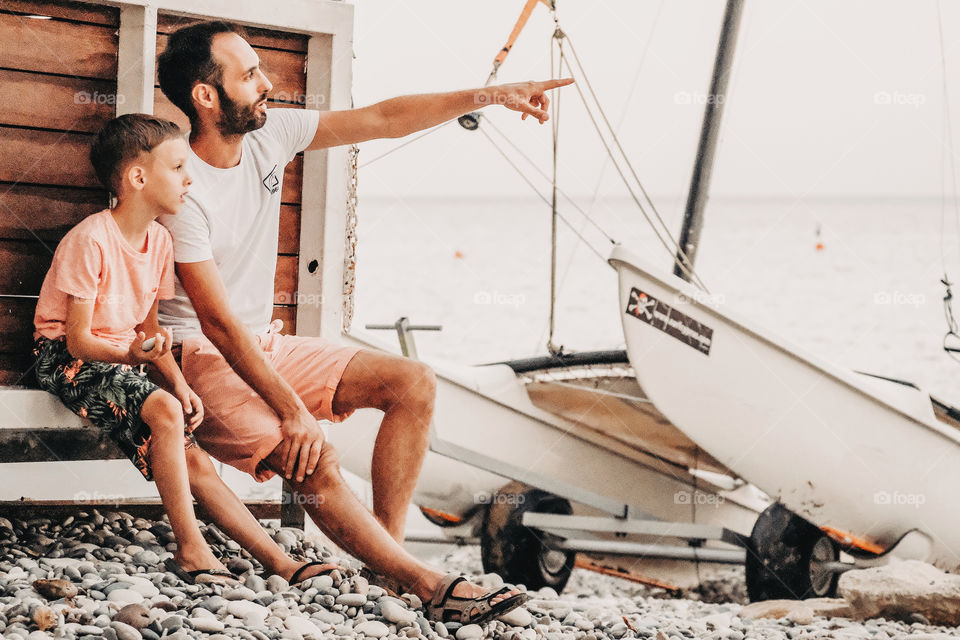 Father and son are sitting on the beach and talking