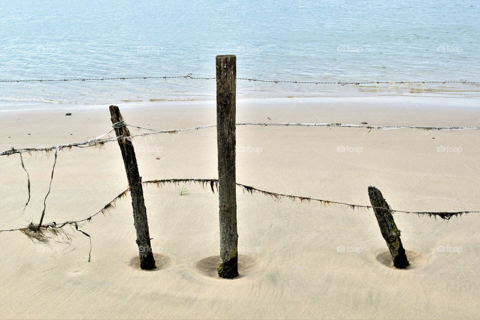 Old weathered wooden poles in sand on the beach with blue water