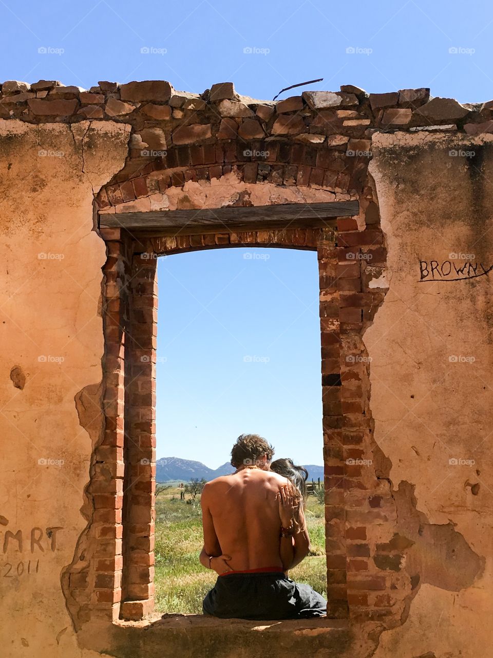 Young lovers in an embrace while sitting in the window frame of an old 100 plus year old stone abandoned settlers house in the Australian outback near the Flinders Ranges 