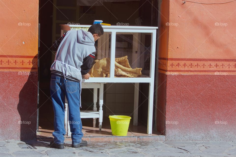 A man is at work washing his glass display case of pork rinds for sale in San Miguel de Allende, Mexico.
