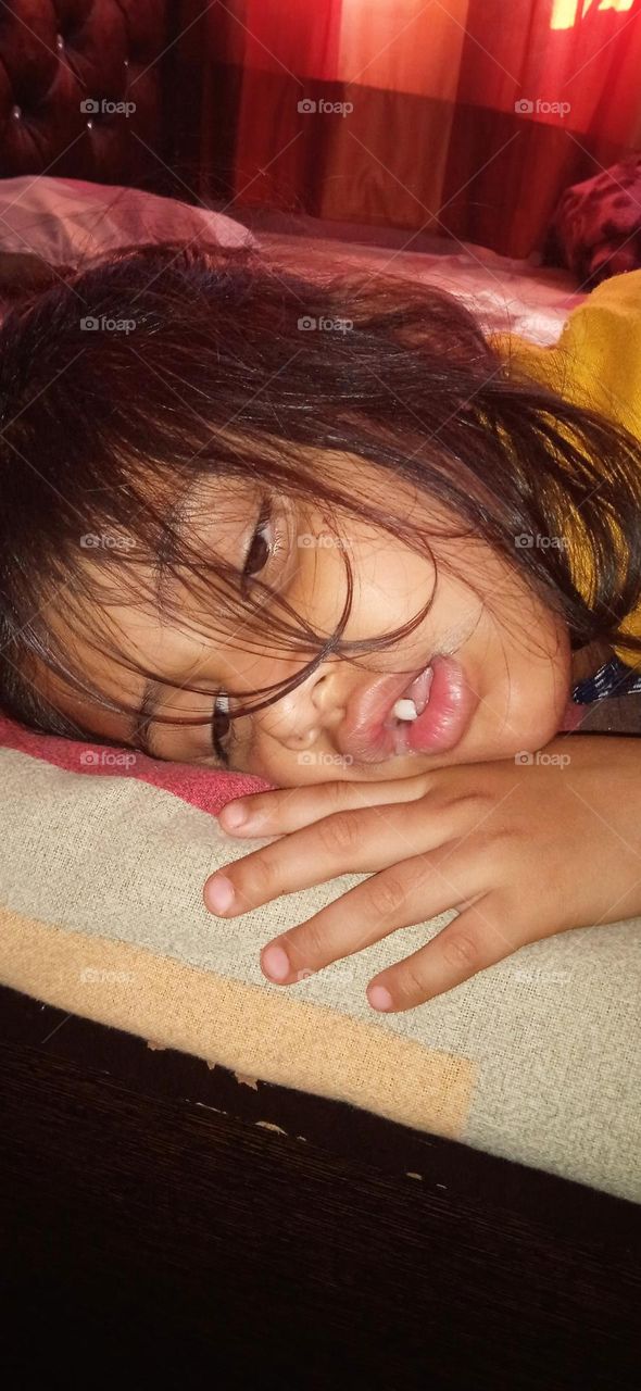 A girl sleep unconsciously, his lovely face covered by hairs and one tooth is shining, his eyes half close looking beautiful, photo shoot  at tue, 2 may, 2023, 6:00 am.