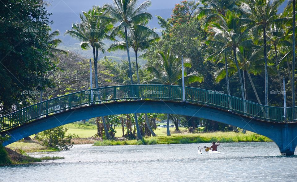 Paddler going under a concrete pony arch bridge over Wailoa River at Wailoa River State Park in Hilo, Hawaii.