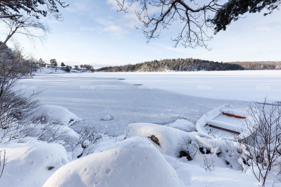 Snow covered forest and rocks, boat in a frozen lake on a cold beautiful winter day 