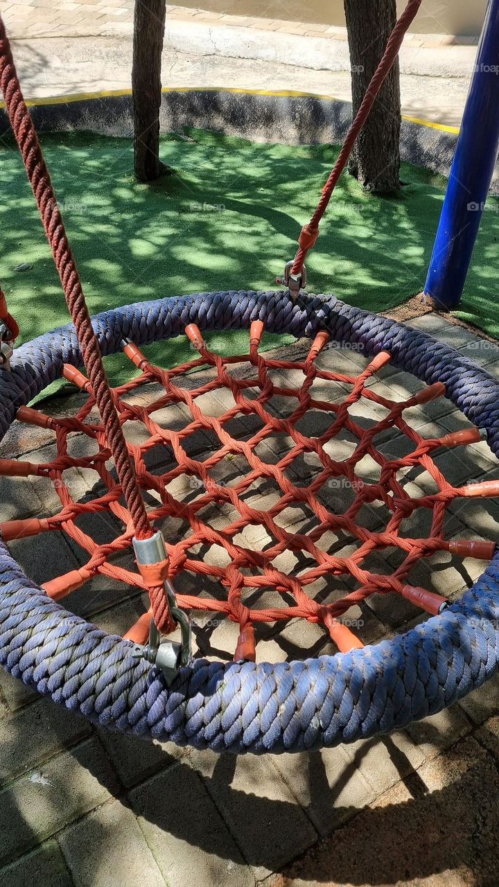 A circular playground swing,made of rope and metal.