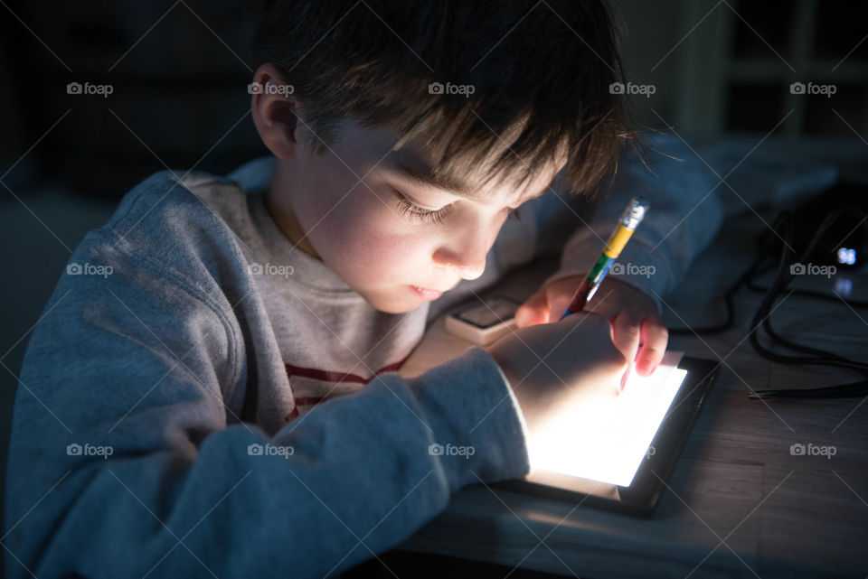 Young boy using an illuminated electronic drawing pad with the light glowing on his face