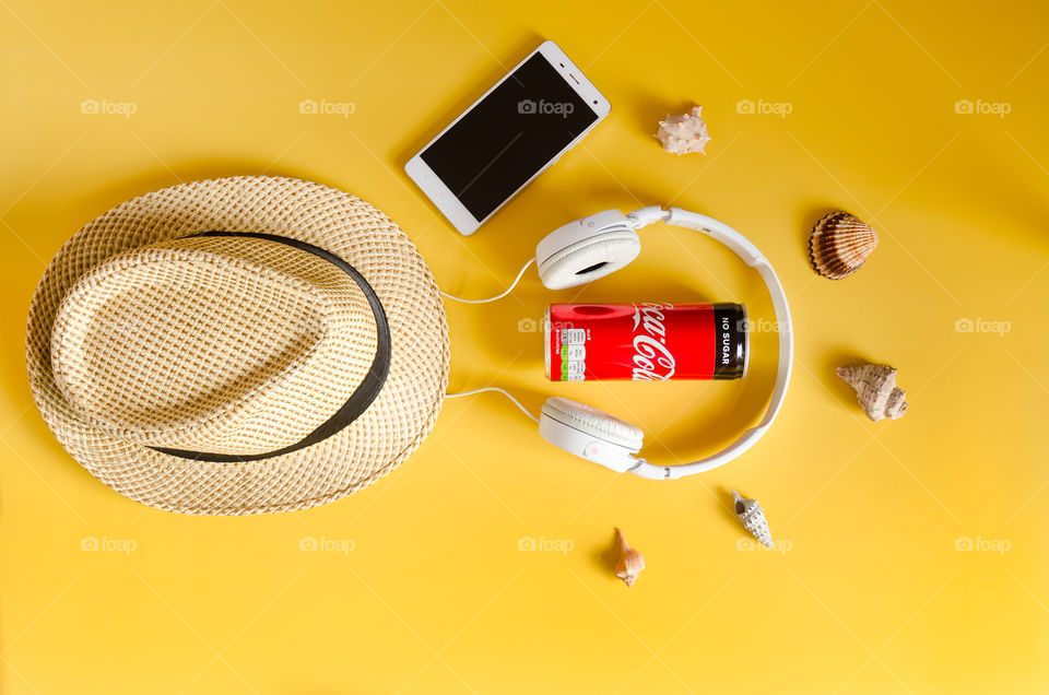 Travel under Covid-19 and new normal concept. Top view of medical face mask, can of Coca-Cola, phone and beach hat on yellow background. Creative ideas of prevent Coronavirus
