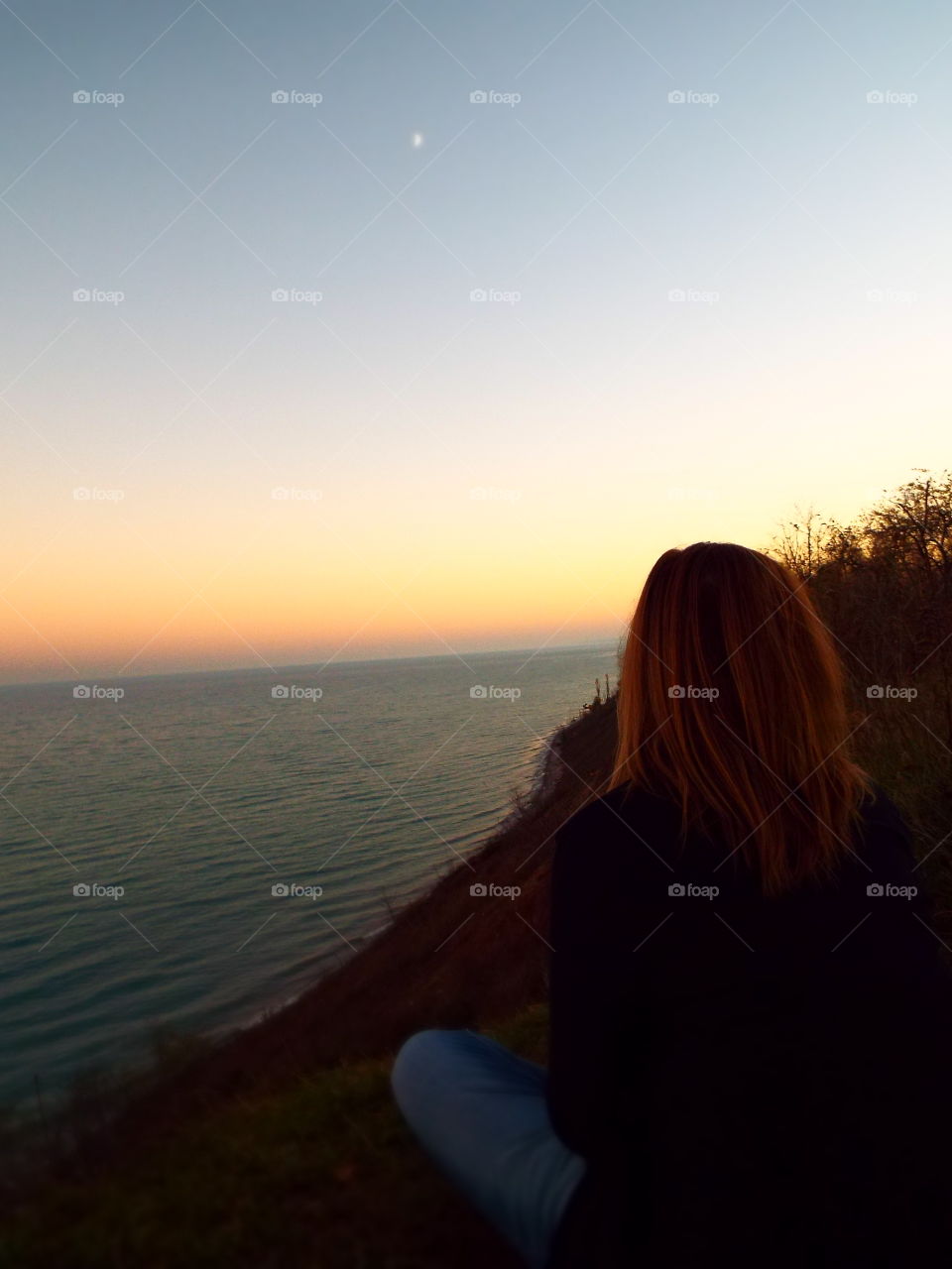 Woman sitting on cliff overlooking Lake Michigan at sunset