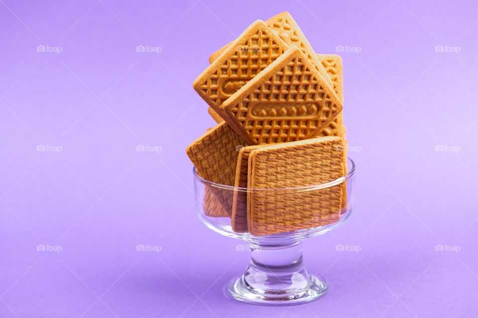 Stack of square biscuits in glass dish on purple background