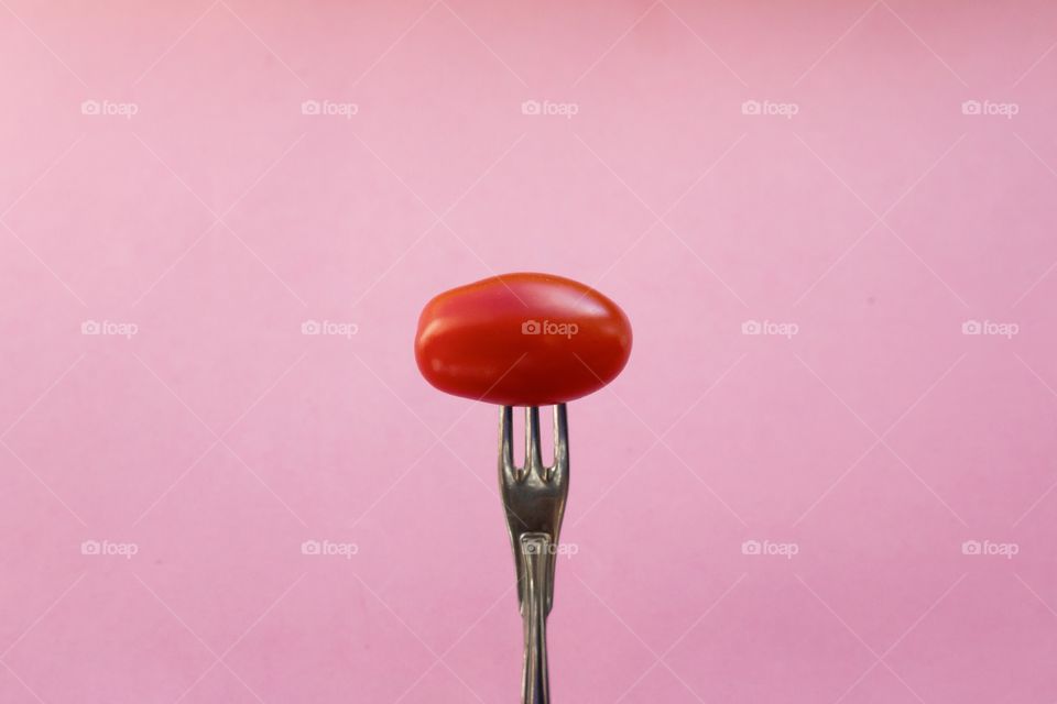 Red tomato on small fork, pink background 