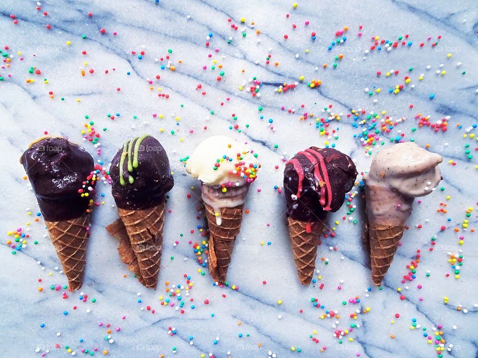 Summer ice cream treats -five ice cream cones flat laid in a straight row, on a marble table scattered with colourful sprinkles. Minimal, overhead shot, copy space