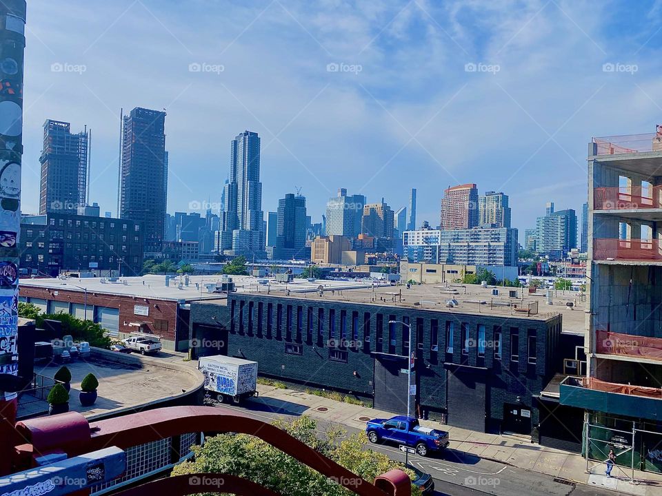Overlooking adjacent flat rooftops in „Greenpoint“, Brooklyn we can see far into the distance from the „Pulaski Bridge“ at „Newtown Creek“, all the way to „Manhattan“ on this beautiful summertime afternoon in 2023. Hypnotic Productions