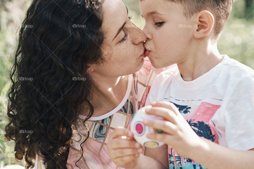 A little boy is very busy with a toy while mom kissing him 😁