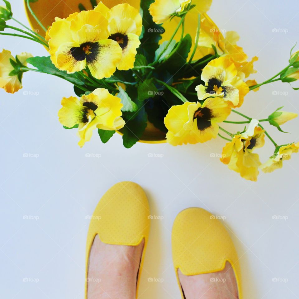 Woman wearing yellow shoes stops to admire yellow flowers in a basket 🧺