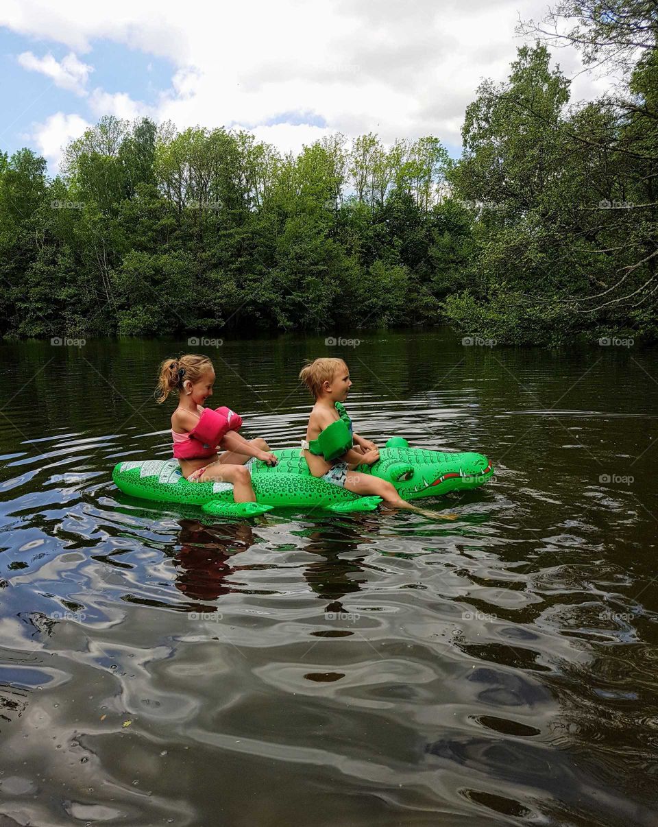 two children floating on a crocodile in forest lake