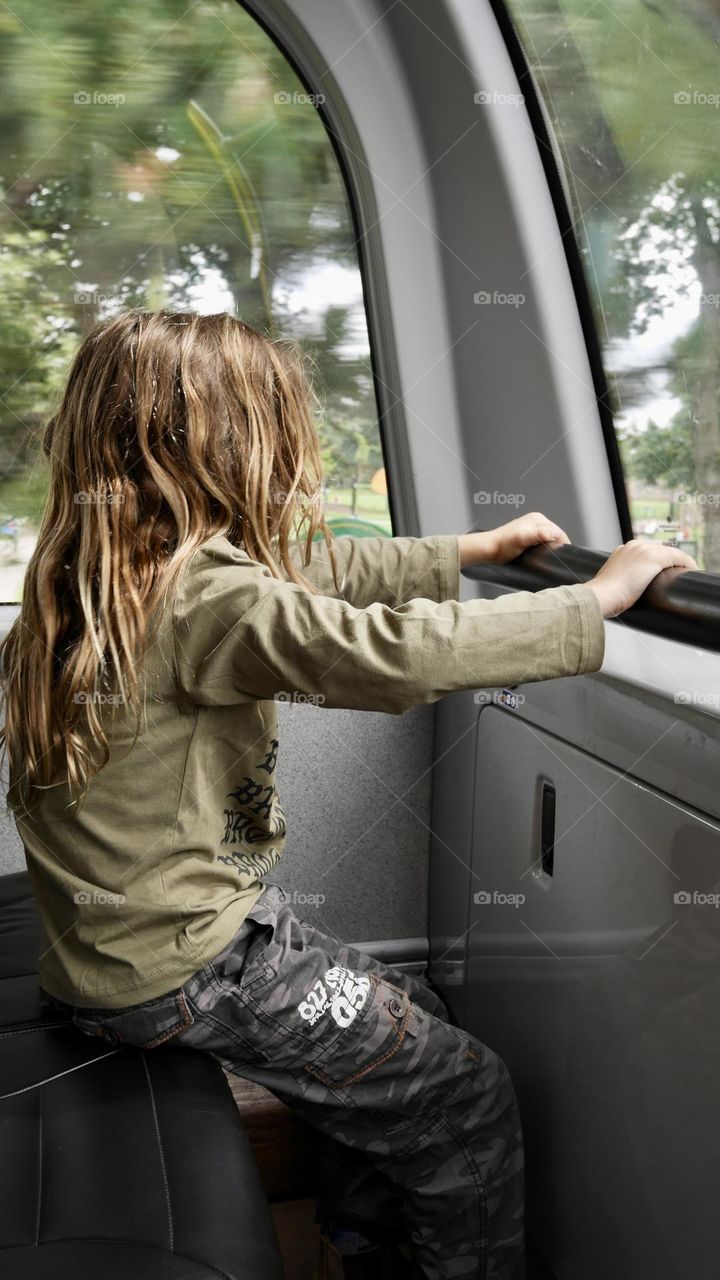 Kid sitting at the upper floor of public double decker bus looking from the window 