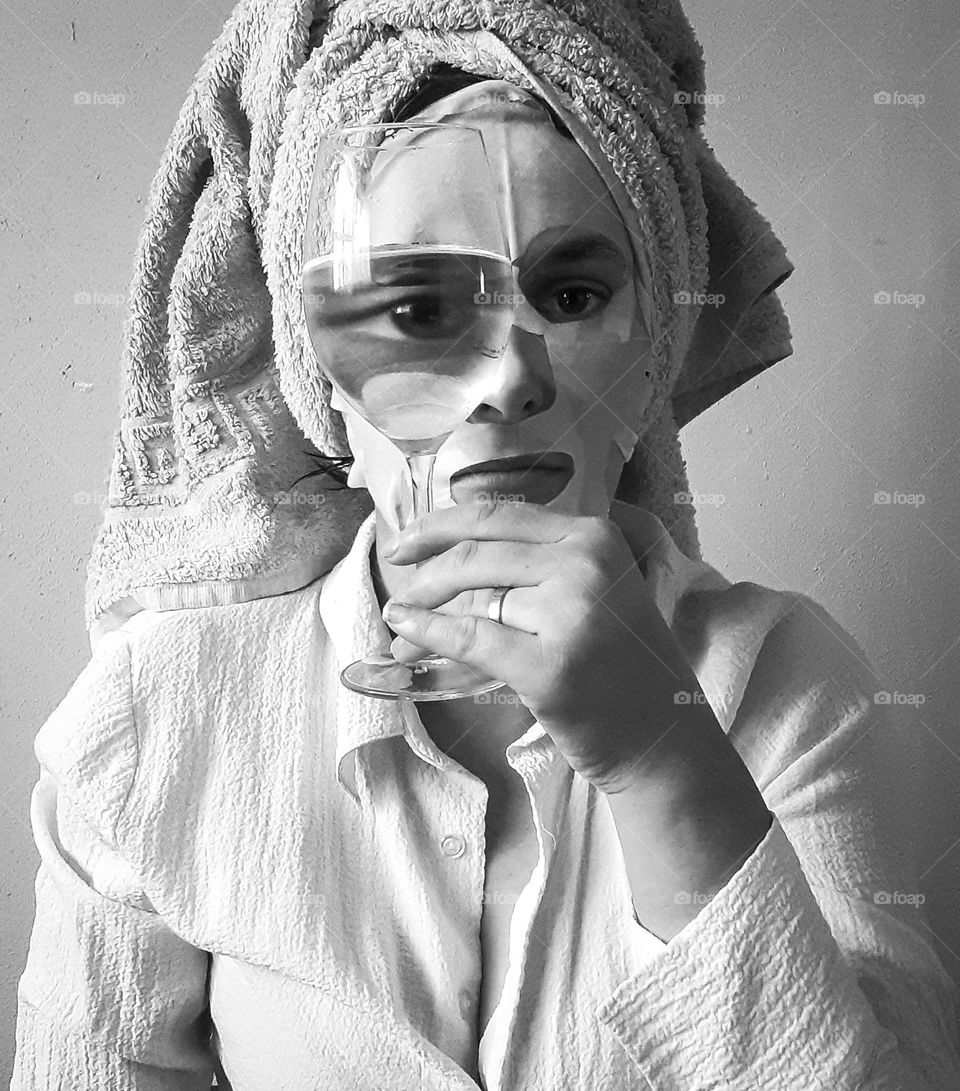 an original, black and white portrait of a girl in a towel with a glass in her hands, in which her eye is reflected