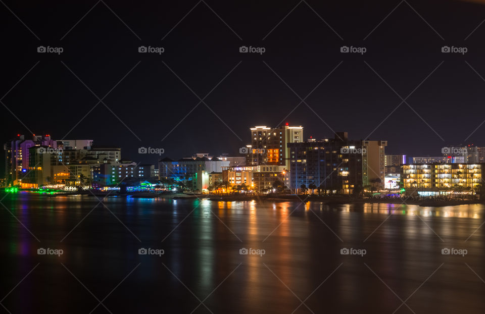 resorts and residences along the waterfront in a beautiful beach area with bright lights on the buildings reflecting on the water