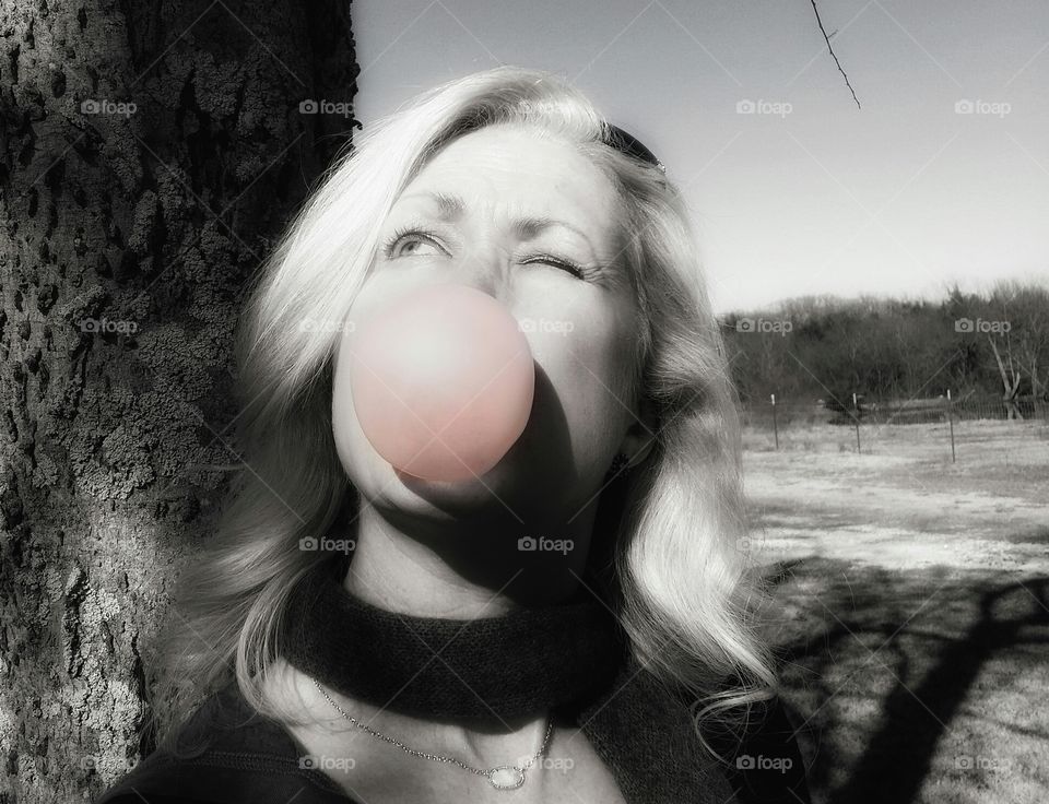 A woman in black and white blowing a pink bubble