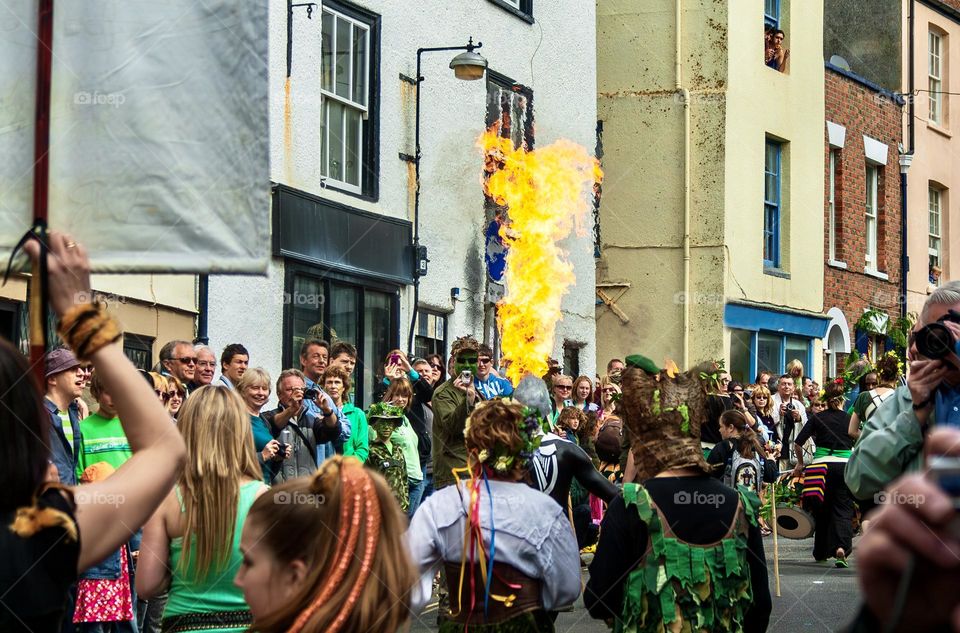 A crowd of people enjoy a procession including a fire breather
