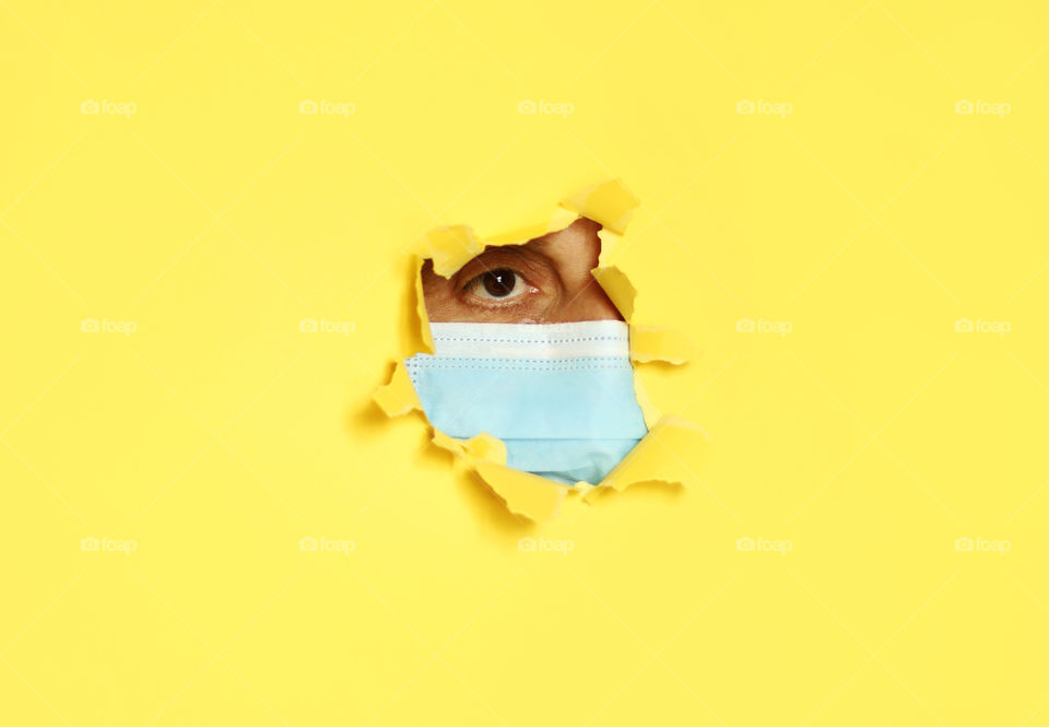 A woman with protective mask behind a hole in yellow paper wall