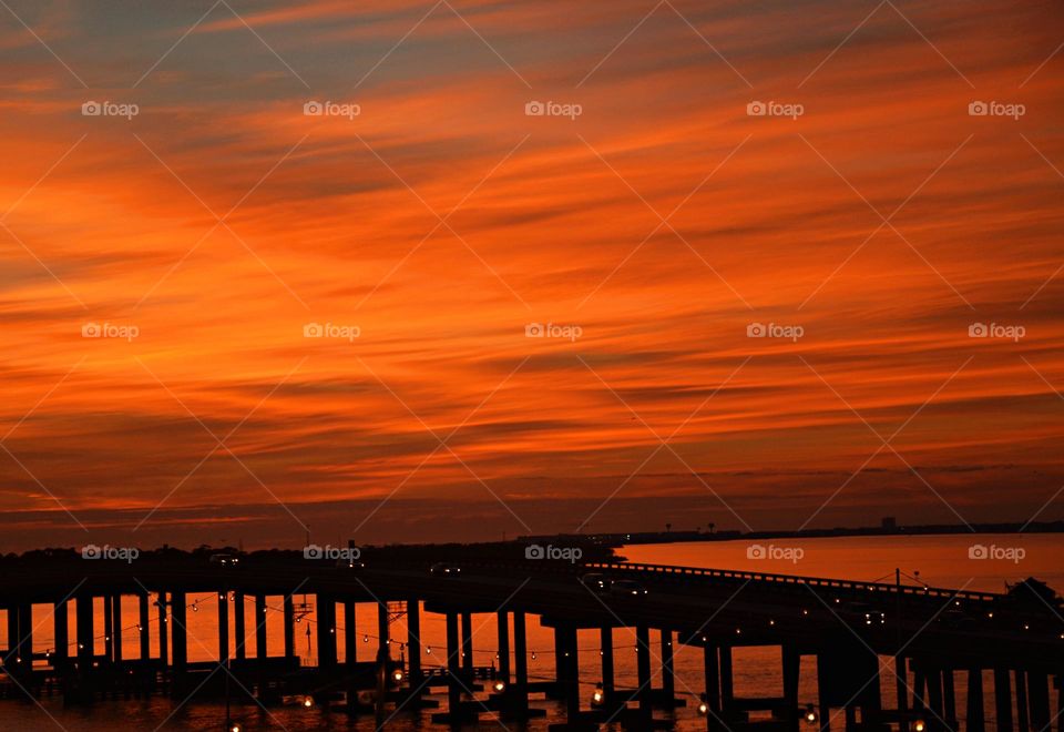 Sunset over the Gulf of Mexico - It was sunset. I watched with an unwavering gaze, as a fiery orange orb of light slowly sink beneath the bridge, and threads of light lingered in the sky, mingling with the clouds