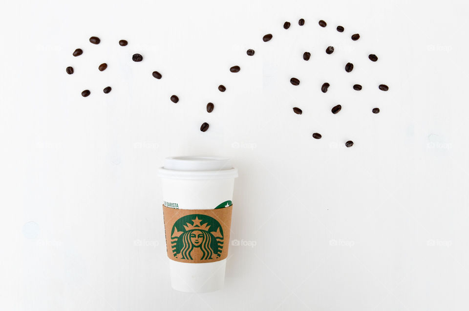 Starbucks coffee cup laid out on a white table with coffee beans appearing to sprout out of the top