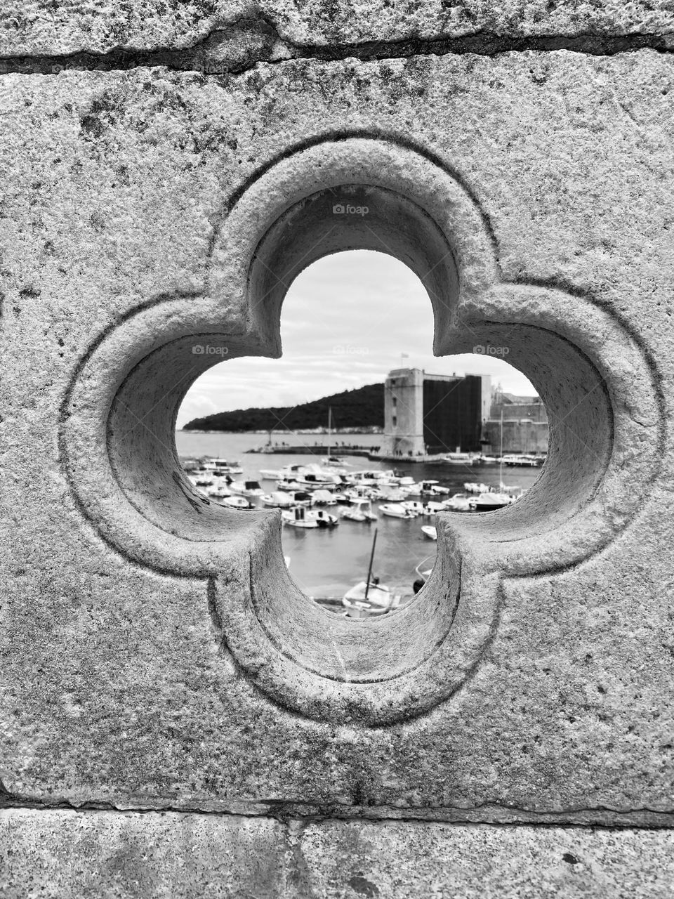 Black and white photo looking through the stone fence at the view of Dubrovnik’s old harbor in Old Town.